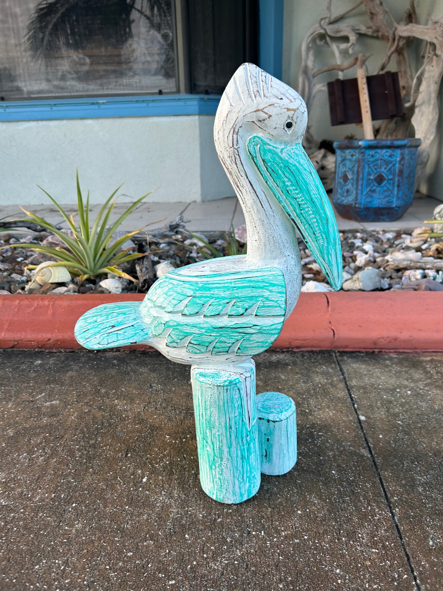Decorative pelican sculpture on a sidewalk with a building and plant in the background