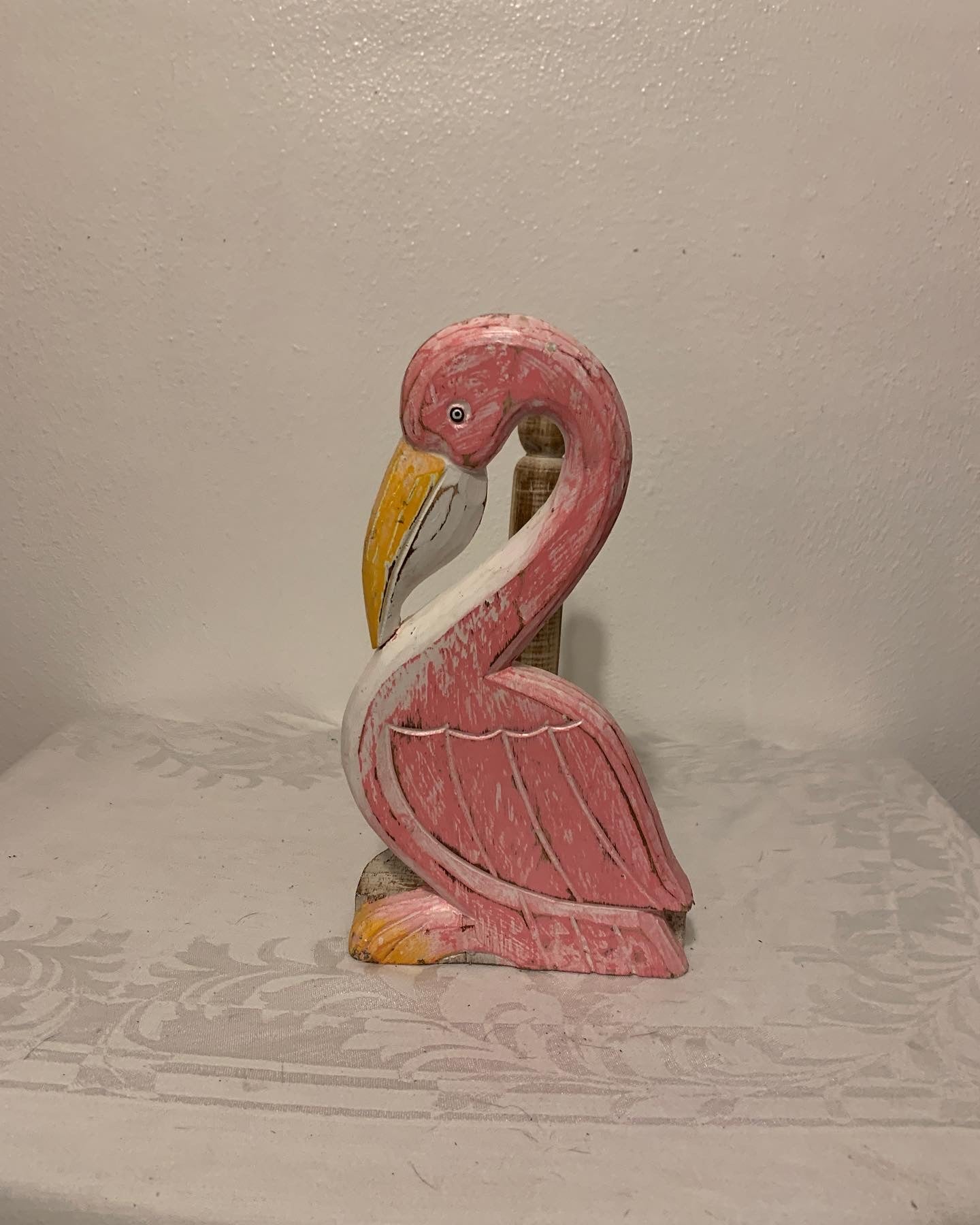 Wooden flamingo figurine on a textured surface with a plain background