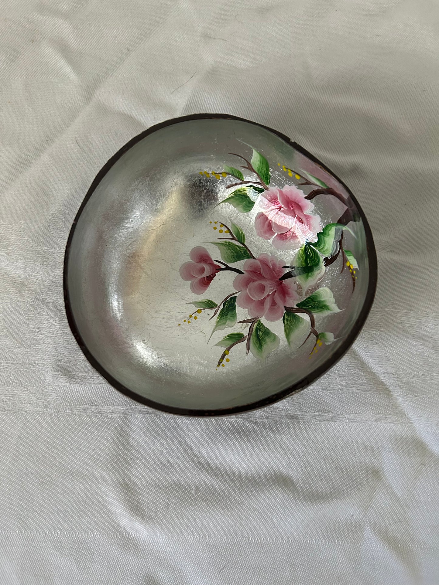 Decorative coconut bowl with floral design on a light fabric background